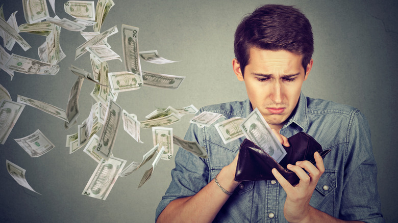 A sad man watching money fly off his wallet
