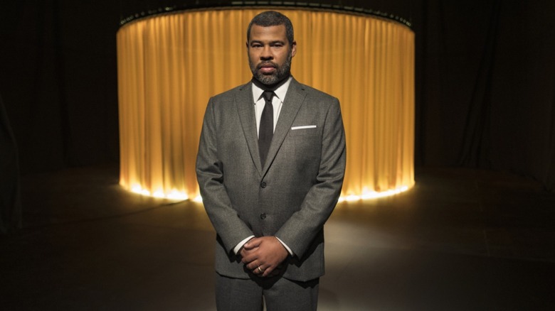 Jordan Peele in a suit stood in front of a light feature in "The Twilight Zone"