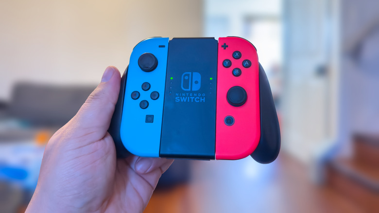 A hand holding a Nintendo Switch controller with blue and red Joy-Con connected to a Joy-Con grip