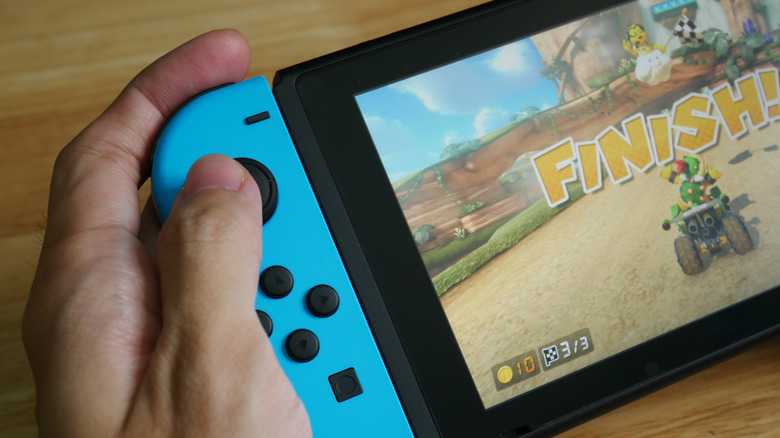 A hand holding a Nintendo 1 Switch with a blue Joy-Con controller