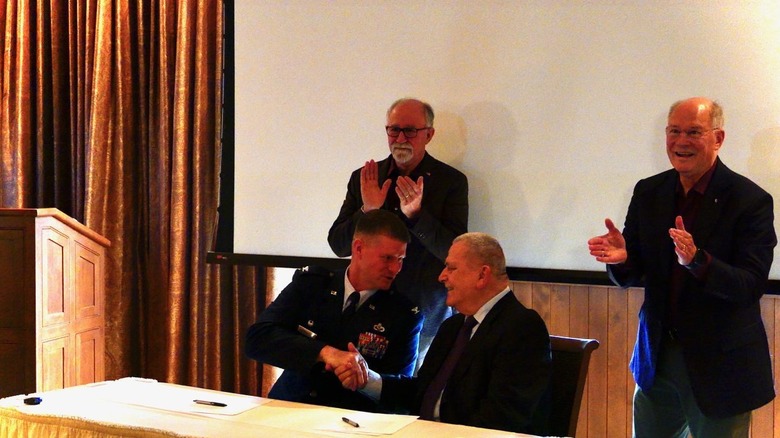 Signees clap as Col Dustin Richards, commander of the Wright Patterson Air Force Base, shakes hands with Air Camp Board President Vince Russo