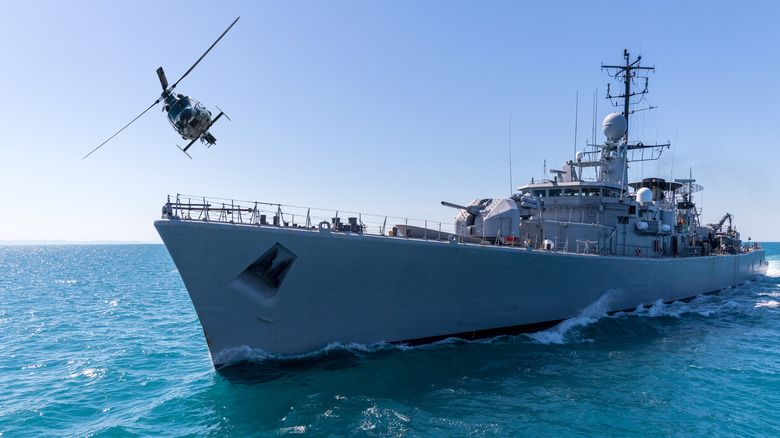 A helicopter flies over the foredeck of a naval destroyer