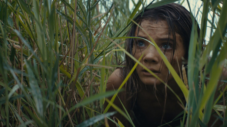 Freya Allan hiding in the grass in Kingdom of the Planet of the Apes