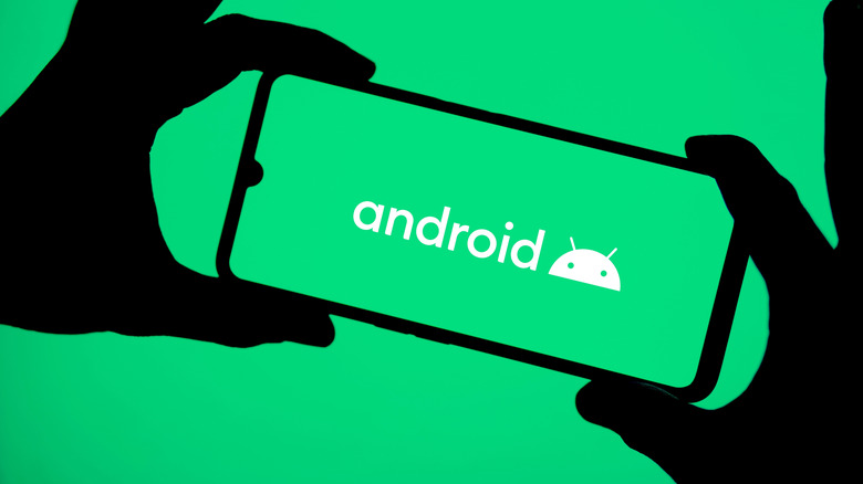 The Android logo on a smartphone being held up by two hands.