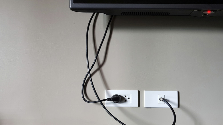 Under a TV showing the power plug in the socket with cables hanging down.
