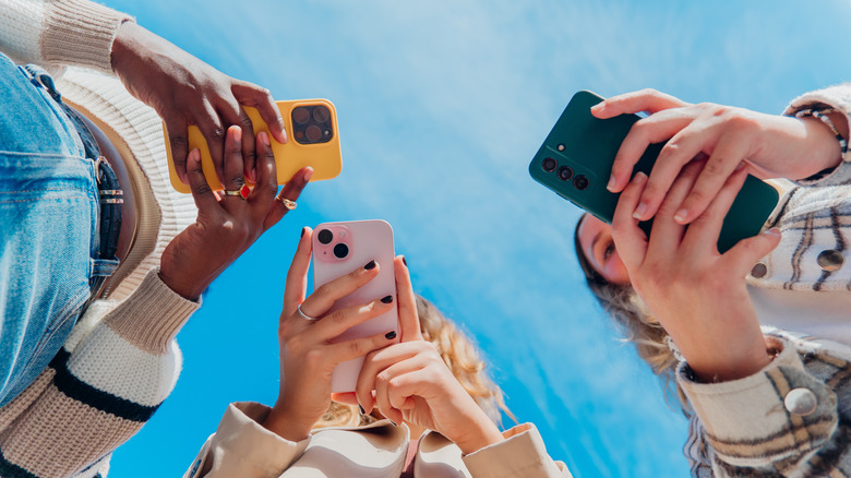 Smartphone users holding Android and iPhone handsets and looking at their displays.