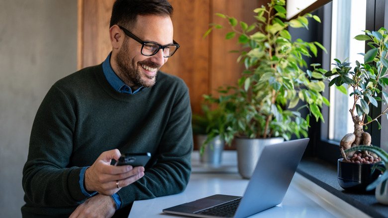 A man looking at his laptop and holding his phone