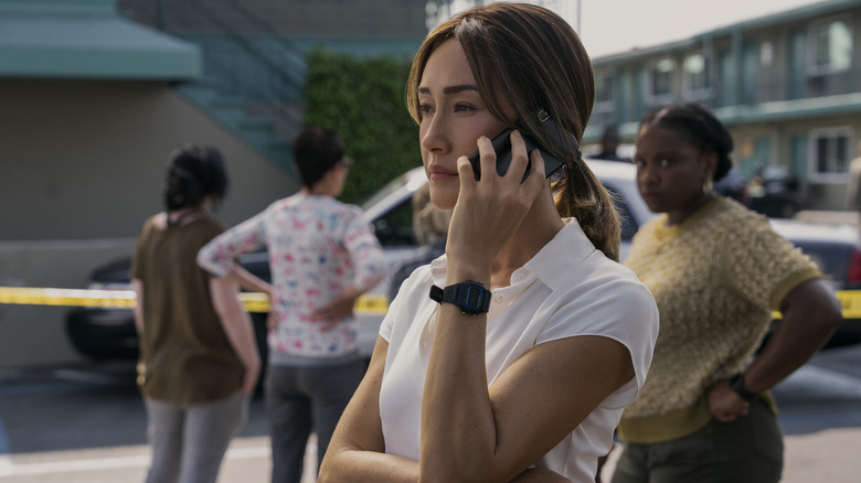 A woman wearing a white shirt holds a phone to her left ear