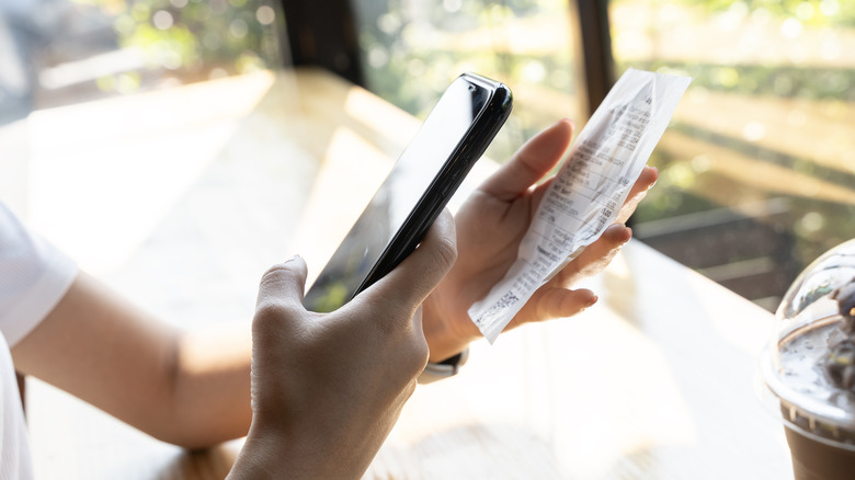 Someone scanning a receipt with their smartphone in the other hand.