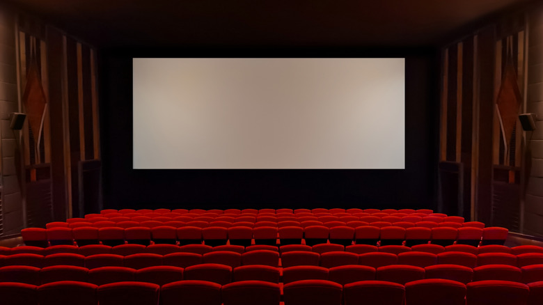 A classic movie theater with red seats, a large screen, and wall speakers.