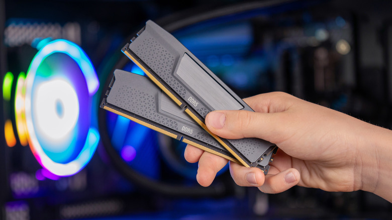 Hand holding two sticks of RAM in front of a gaming PC