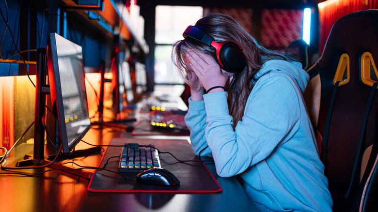 Person sat at computer wearing headset, with head in their hands