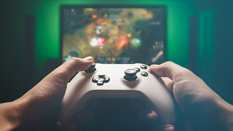 Person holding an Xbox controller in front of a TV screen
