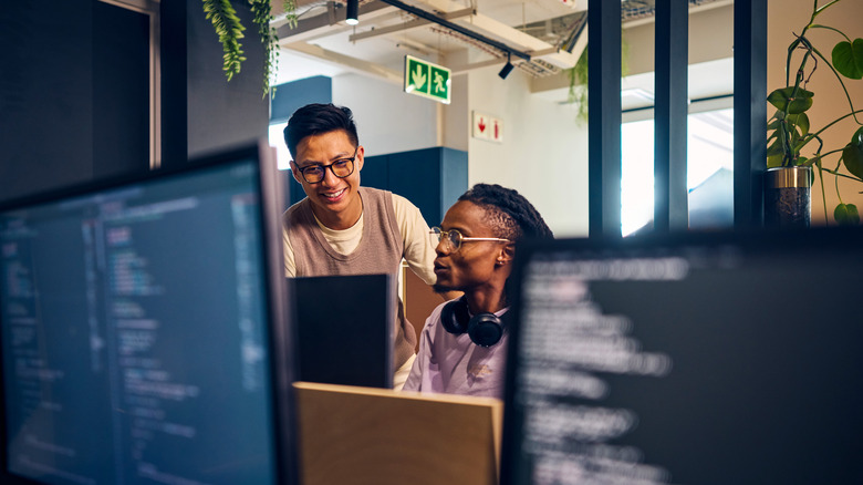 Two employees discussing something in front of a computer monitor in an office building.
