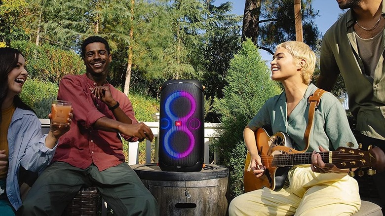 The JBL PartyBox 110 being used as a guitar amplifier by a group of people in an outdoor setting.