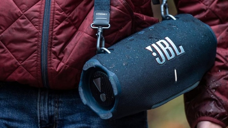 A person has the JBL Xtreme 4 slung over their shoulder with the carrying strap.
