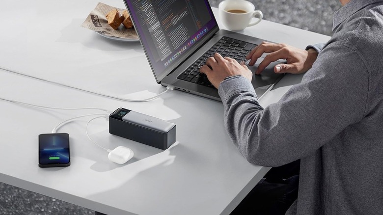 A person using the Anker 737 Portable Charger for a laptop, phone, and earbuds case.