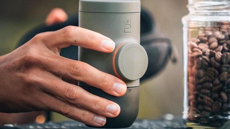 Minipresso GR2 in someone's hand next to jar of coffee beans