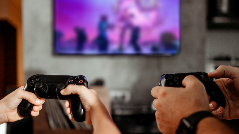 Two people holding gaming controllers in front of a TV.