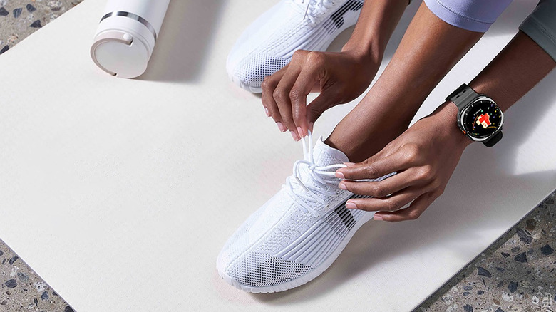 A woman's foot on a yoga mat, her hands tying the laces while wearing a Samsung Galaxy Watch Ultra.