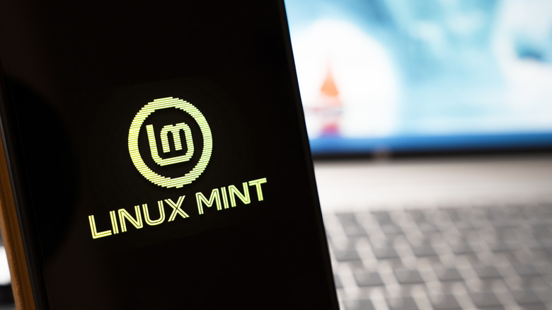 A phone with the Linux Mint logo with a blurred laptop seen in the background.