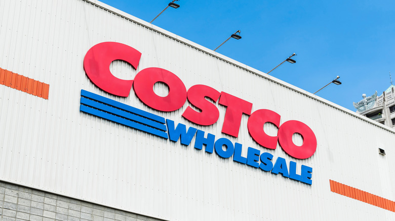 An exterior shot of a Costco Wholesale warehouse, the image prominently displays the Costco Wholesale logo