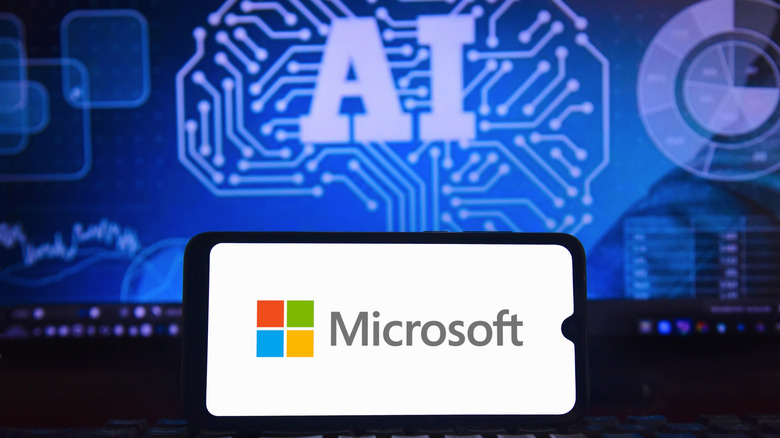 The Microsoft logo displayed on a smartphone in front of a monitor with an AI graphic