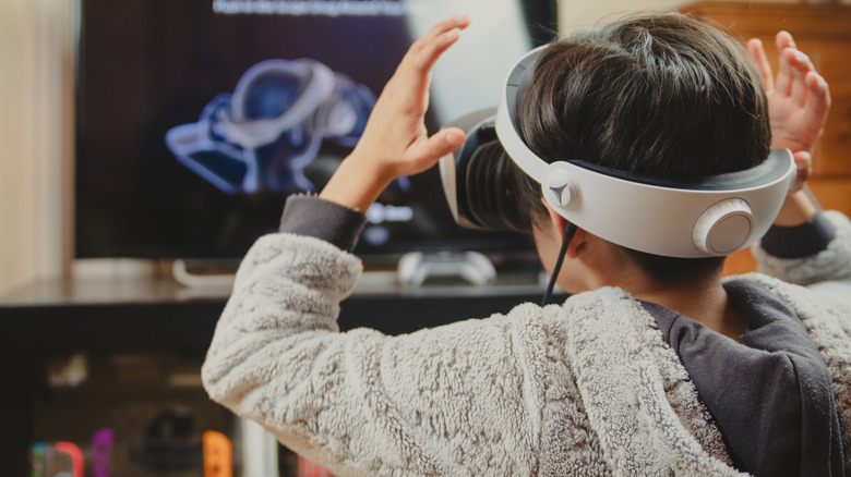 Person using a PlayStation VR2 headset in front of a TV.