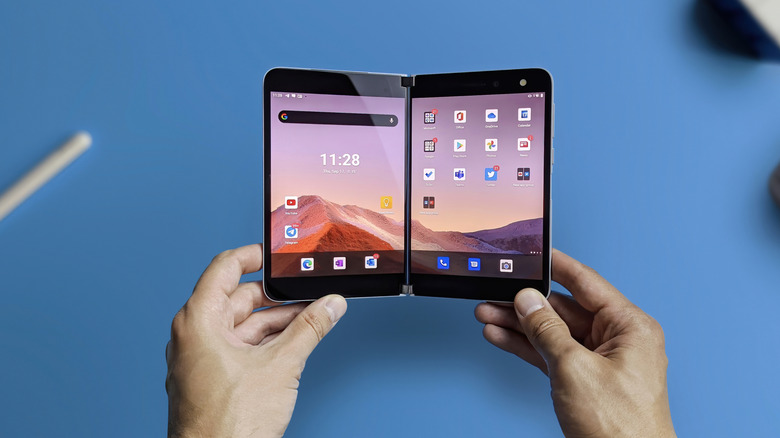 Microsoft Surface Duo held open with two screens on a blue background.