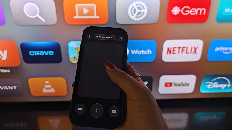An iPhone being held up to a TV showing Apple TV icons, the iPhone displaying a remote pad.