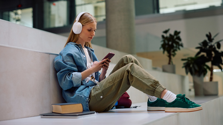 A person with headphones sitting on stairs a with phone and books