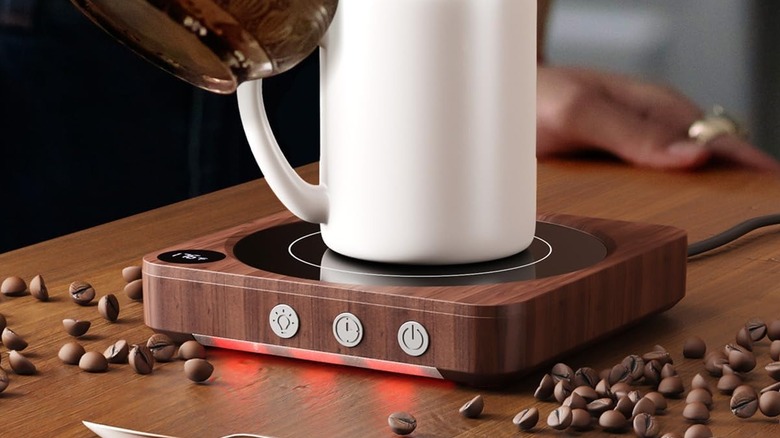 A white mug sits on top of a House Gem Mug Warmer as a person pours coffee into it.