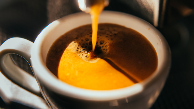 An espresso machine pours espresso into a white mug.