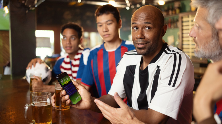 A group of friends looking at sports scores on a phone while in a bar.