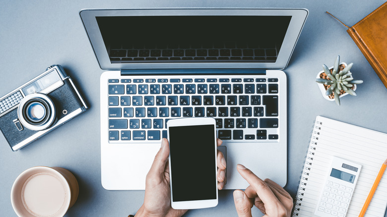 A person holding a smartphone over a laptop