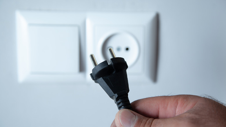 Hand holding a UK power cable with a UK wall outlet in the background