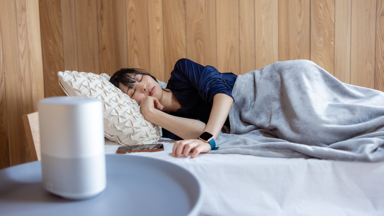 a woman sleeping with a speaker on the nightstand