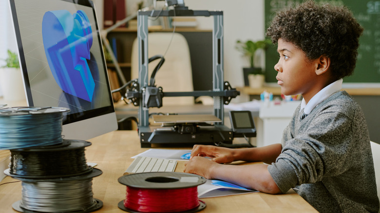 Young boy using modeling software with 3D printing filament in the foreground.