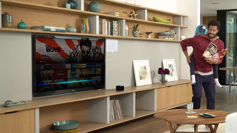 A man and his child walking by a living room TV that uses the Fire TV interface.
