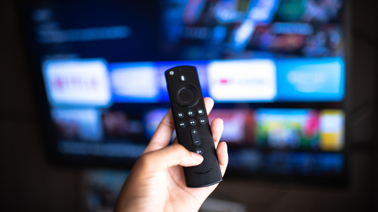 A person holding the Amazon Fire TV Stick remote with an out of focus view of a TV in the background