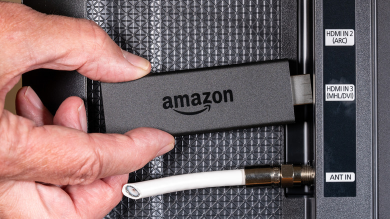 A close up of a person inserting an Amazon Fire TV Stick into a TV's HDMI port