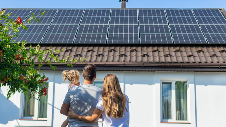 A family stands in front of their house looking at the solar panels on the roof