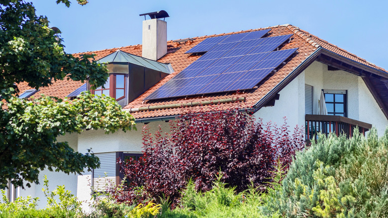 Attractive house with solar panels on red tiled roof with a leafy garden in the foreground.
