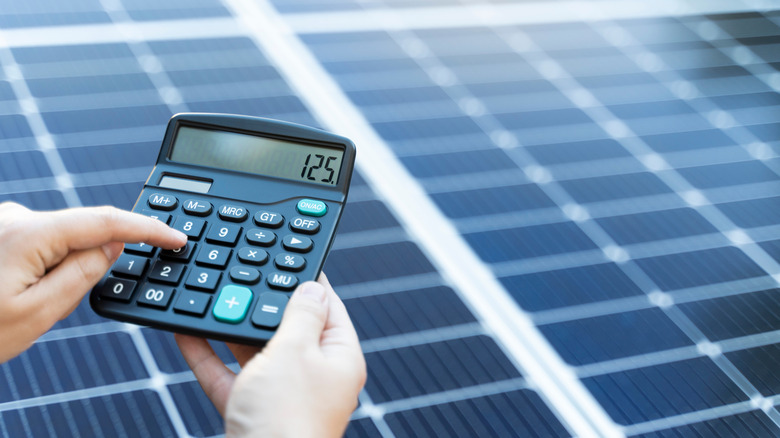 Hands holding a calculator in front of blurred solar panels.