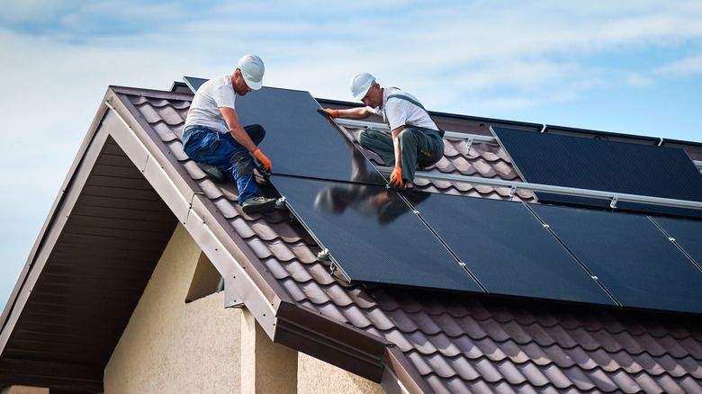 Workers installing solar panel system on rooftop of a house.