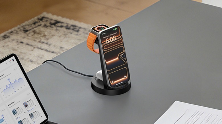 The Anlmz 3-in-1 Charging Station sitting on a grey desk next to a laptop and some papers, it is charging an iPhone, an Apple Watch, and a pair of AirPods