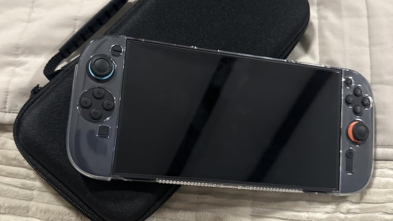 A black Nintendo Switch 2 sitting on a bed with white bedsheets, the console is using accessories from the Binbok 18-in-1 Nintendo Switch 2 bundle