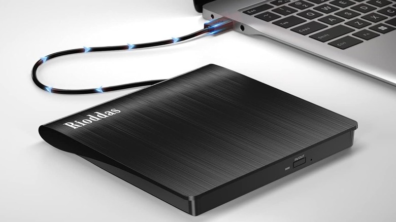 The Rioddas External CD/DVD Disk Reader Drive connected to a grey Windows laptop, computer generated effects are embedded over the cable, likely indicating the drive sending information to the laptop