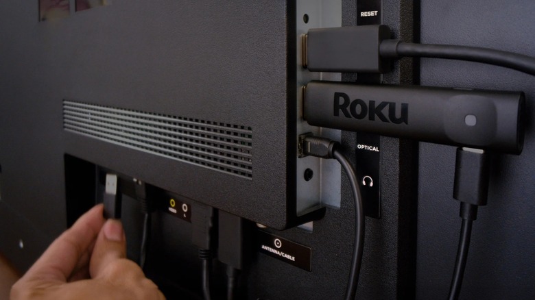 A person powering a Roku Streaming Stick via a TV's USB port