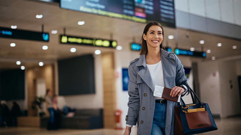 Woman walking through airport, departure board visible in the background